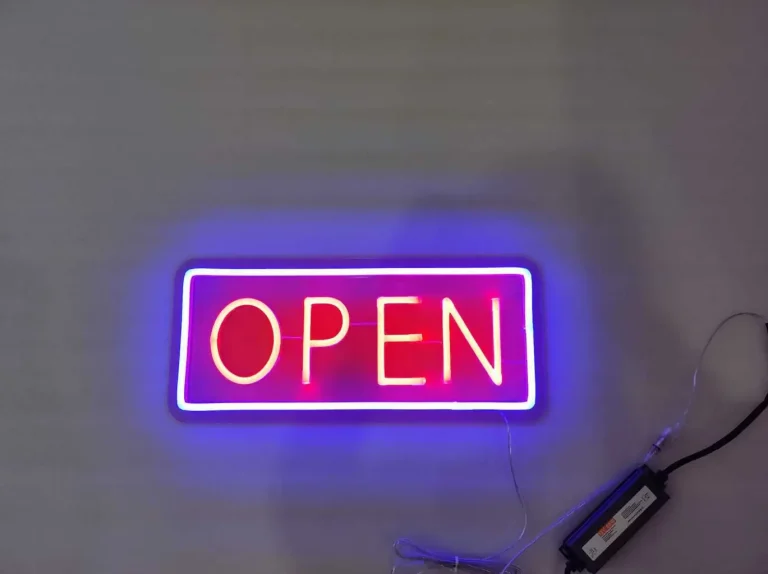 Bright green LED neon sign spelling THE KOKO SHOW on a red brick wall illuminating a podcast studio with three hosts