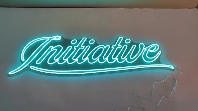 Aqua script LED neon sign reading Initiative mounted on a textured wall ideal for a business in Australia