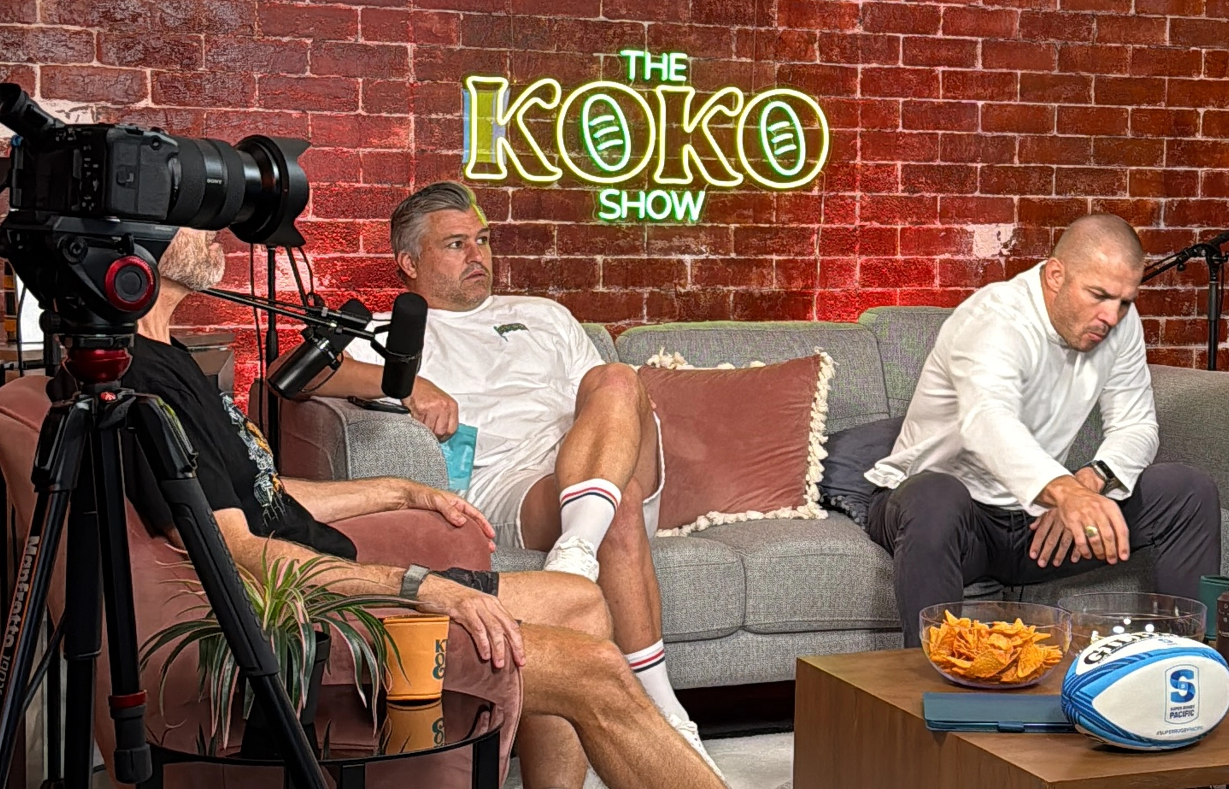 Green LED neon sign spelling 'THE KOKO SHOW' on a red brick wall in a podcast studio Australia