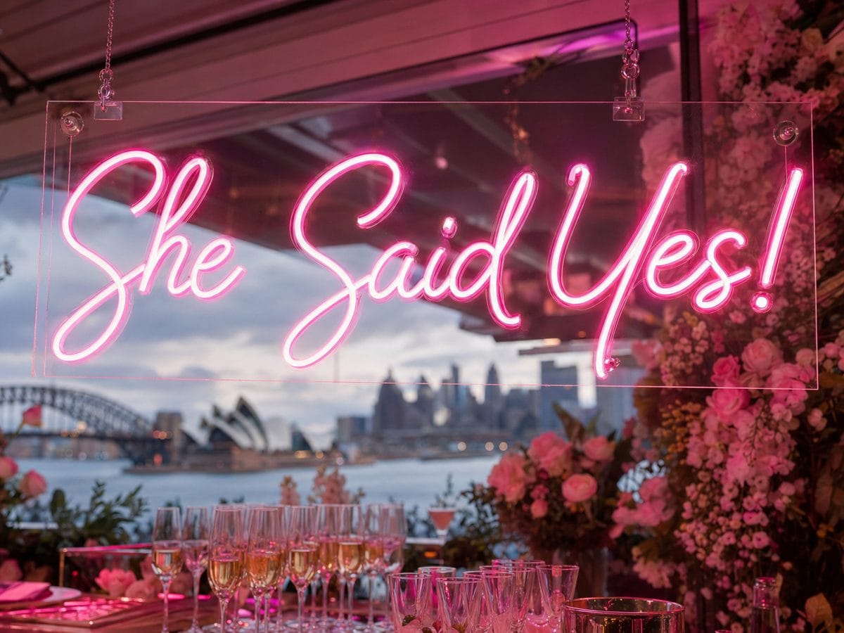 She Said Yes pink LED neon sign at a Sydney engagement party with Harbour Bridge and Opera House view 2026