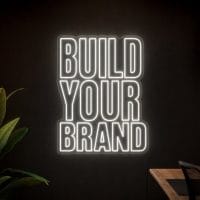 Build Your Brand Neon Sign Build Your Brand LED neon sign in white in startup office studio with modern creator environment