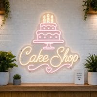 Cake Shop LED neon sign with tiered birthday cake icon on clear acrylic backing mounted on white brick wall