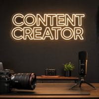 Content Creator LED neon sign in warm white above camera desk in minimalist creator setup