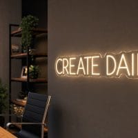Create Daily LED neon sign in warm white in minimalist office aesthetic with content creator desk