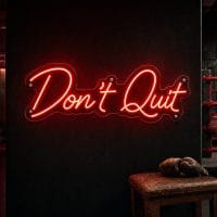 A vibrant red "Don't Quit" neon sign mounted on a dark, moody training space wall, glowing intensely.