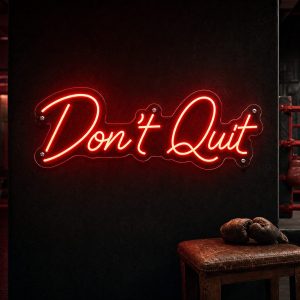 A vibrant red "Don't Quit" neon sign mounted on a dark, moody training space wall, glowing intensely.