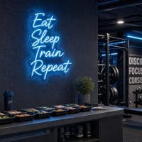 An Ice Blue 'Eat Sleep Train Repeat' neon sign mounted on a dark, moody training space wall, with cinematic lighting.