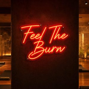A red 'Feel The Burn' neon sign mounted on a dark wall in a moody training space, with cinematic lighting highlighting the sign's glow.