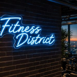 An Ice Blue 'Fitness District' neon sign mounted on a dark grey wall in a modern, LED-lit fitness room with exercise equipment in the background.