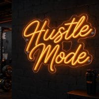 An orange 'Hustle Mode' neon sign mounted on a dark, textured wall in a concrete industrial gym, with gym equipment visible in the background.