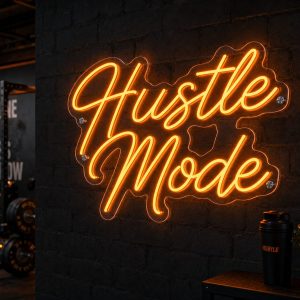An orange 'Hustle Mode' neon sign mounted on a dark, textured wall in a concrete industrial gym, with gym equipment visible in the background.