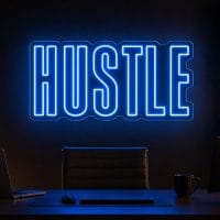 Hustle LED neon sign in electric blue in dark moody office studio with luxury desk setup