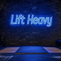 A blue "Lift Heavy" neon sign mounted on a concrete wall in an industrial gym setting.