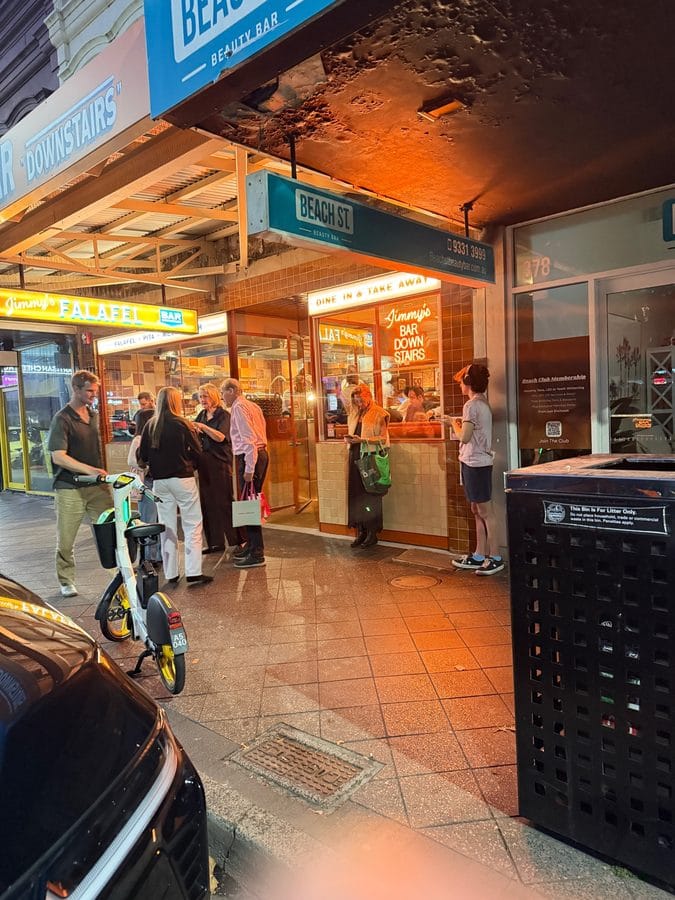 Neon sign for falafel bar glowing at night in Sydney Australia with people outside