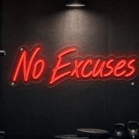 Red 'No Excuses' neon sign mounted on a dark moody training space wall with cinematic lighting.
