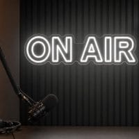 On Air LED neon sign in white mounted behind podcast desk with luxury black wall and microphone setup