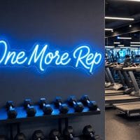 A vibrant Ice Blue 'One More Rep' neon sign mounted on a dark, textured wall in a modern home gym with exercise equipment.