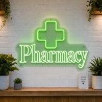 Pharmacy LED neon sign with green medical cross icon on clear acrylic backing mounted on white brick wall