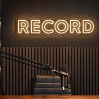 Record LED neon sign in warm white beside microphone arm in cinematic podcast room