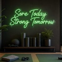 A vibrant green 'Sore Today Strong Tomorrow' neon sign mounted on a concrete industrial gym wall, with cinematic lighting and a realistic LED glow.