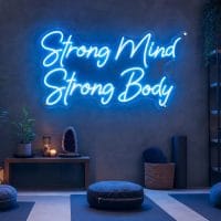 An Ice Blue neon sign displaying 'Strong Mind Strong Body' mounted on a dark grey wall in a modern, moody training space, with cinematic lighting.