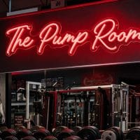 Red 'The Pump Room' neon sign mounted on a dark, moody training space wall with cinematic lighting.