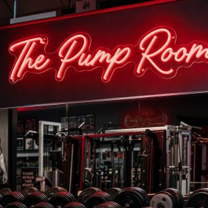 Red 'The Pump Room' neon sign mounted on a dark, moody training space wall with cinematic lighting.