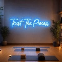 Ice Blue 'Trust The Process' neon sign mounted on a dark wall in a modern home gym with exercise equipment in the background, cinematic lighting.