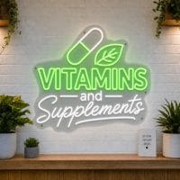 Vitamins and Supplements LED neon sign with pill capsule and leaf icons on clear acrylic backing mounted on white brick wall